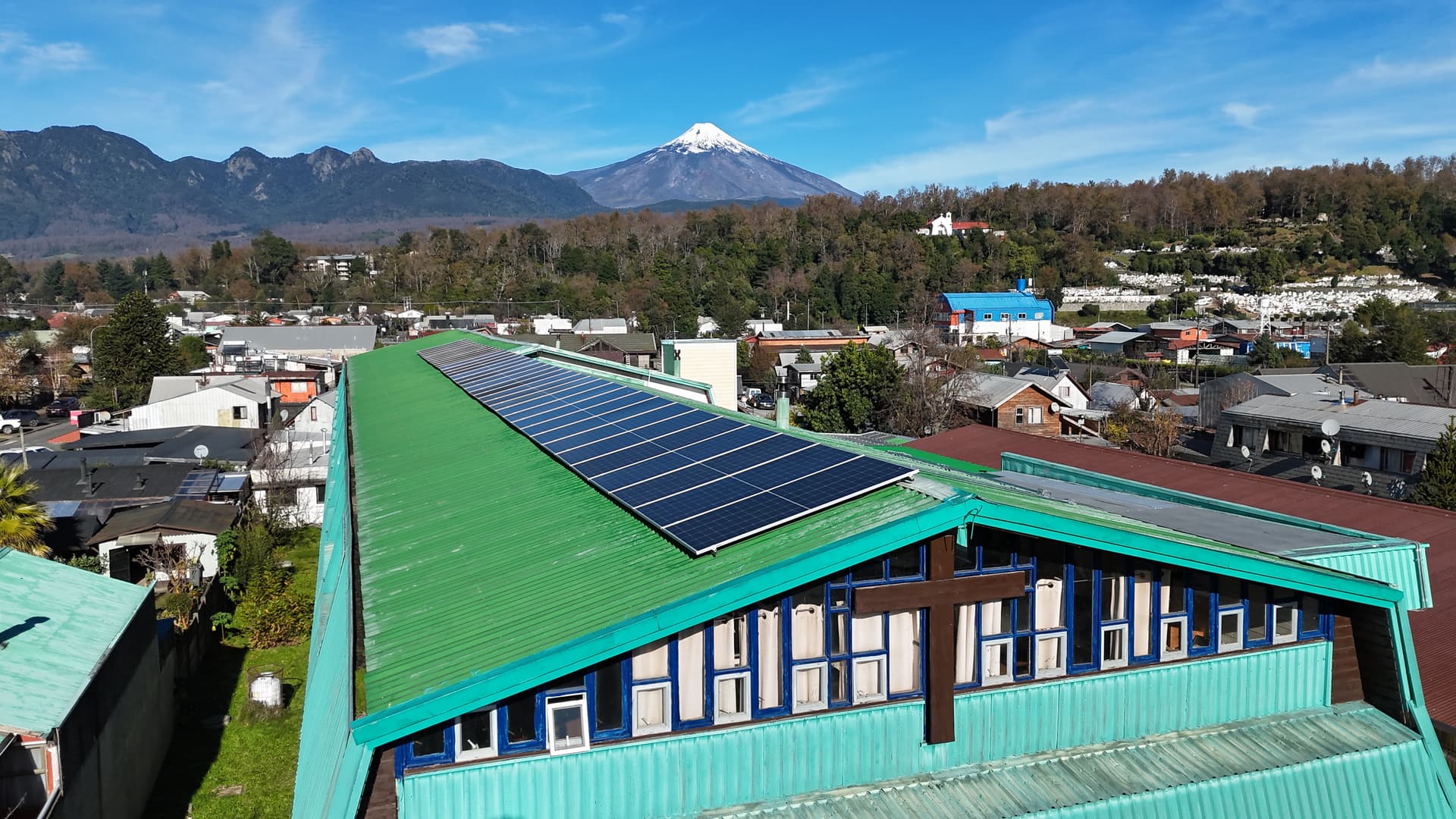 Vista aérea de paneles solares instalados por SolarPro en la techumbre de un colegio de Villarrica, con el volcán de fondo